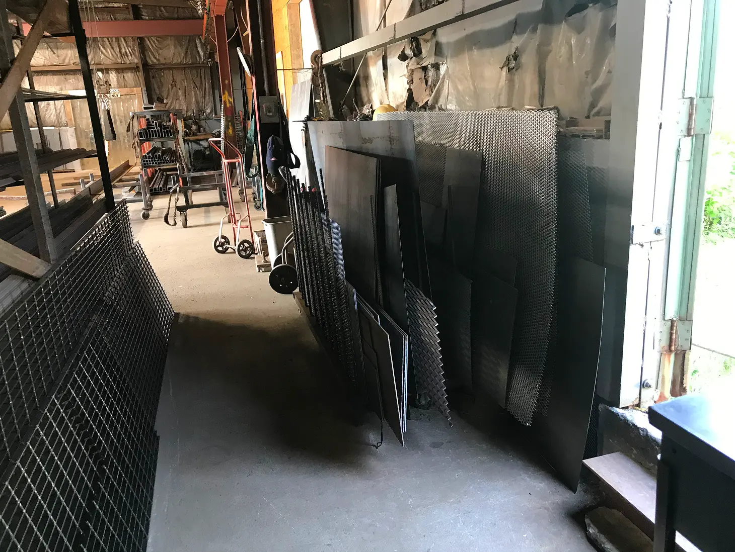 Room filled with lots of metal sheets, a trolley, a desk, a ladder, and other objects